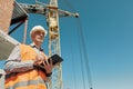 An engineer in an orange vest and a white construction control helmet conducts an inspection with a tablet in his hands Royalty Free Stock Photo