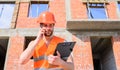 Engineer phone call control process. Guy protective helmet stand in front of building made out of red bricks. Builder