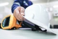 The engineer picks up the white helmet placed on the office desk with a blurred background