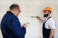 Engineer and project manager with his colleague, construction worker is measuring wall using spirit level tool. Royalty Free Stock Photo