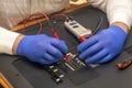 Engineer in service center repairs an LCD TV. Gloved hands measure the resistance on back of the monitor with multimeter.