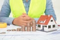 The engineer sits in front of a table with drawings and a small house model and a row of dollar coins