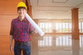 Engineer smile in decorate Interior room completed with hand holding rolled blueprints and wear yellow helmet