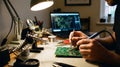 Engineer Soldering Electronic Components onto a Circuit Board at a Workbench with a Laptop Royalty Free Stock Photo