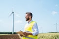 An engineer standing on a field on wind farm, making notes.