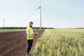 An engineer standing on a field on wind farm, making notes.