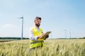 An engineer standing on a field on wind farm, making notes.