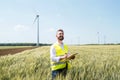 An engineer standing on a field on wind farm, making notes.