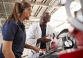 Engineer talking to female apprentice by machinery, close up