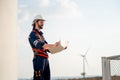 Engineer or technician man stand with holding drawiing paper and look forward also stand in front of windmill or wind turbine Royalty Free Stock Photo