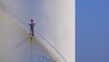 Engineer is walking up spiral staircase to working on top of fuel tank with blue sky background