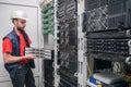 An engineer in a white helmet mounts a stack of switches in a rack. The technician works in the server room. A man installs new Royalty Free Stock Photo