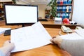 Engineer work place with blueprints, telephone and blank white display of pc monitor, first person view with human hands Royalty Free Stock Photo