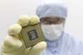 An engineer working in a clear room wearing a special uniform and protective glasses holds processor cpu in hand in glove Royalty Free Stock Photo