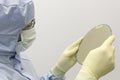 An engineer working in a clear room wearing a special uniform and protective glasses holds silicon wafer with microchips in hand