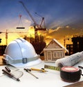 engineer working table plan, home model and writing tool equipment against building construction crane with evening dusky sky Royalty Free Stock Photo