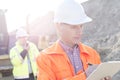 Engineer writing on clipboard at construction site with colleague in background