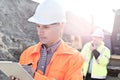 Engineer writing on clipboard at construction site with colleague in background