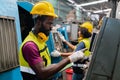 Engineering male African American workers wear soundproof headphones and yellow helmet holding tablet working at operating CNC. Royalty Free Stock Photo