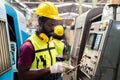 Engineering male african american workers wear soundproof headphones and yellow helmet holding tablet working at operating CNC Royalty Free Stock Photo