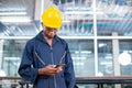 Engineering male african american workers wear soundproof headphones and yellow helmet using work smartphone.
