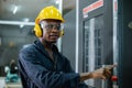 Engineering male african american workers wear soundproof headphones and yellow helmet working at operating CNC machine.