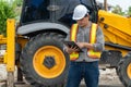 Engineering wearing a white safety helmet standing In front of the backhoe And are using tablet for check the blueprint with const Royalty Free Stock Photo