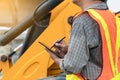 Engineering wearing a white safety helmet standing In front of the backhoe And are using tablet for check the blueprint with const Royalty Free Stock Photo