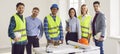 Engineers and architects standing on a building site with architectural plan and smiling Royalty Free Stock Photo