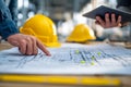 Engineers discussing detailed construction plans with safety helmets on table and digital tablet in an industrial work environment Royalty Free Stock Photo