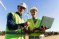 Engineers using laptops to communicate while standing in front of wind turbines.