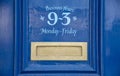 Blue office door with opening times and a brass letterbox.