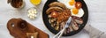 English breakfast in a frying pan with fried eggs, bacon, sausages, beans and toasts on white wooden surface, overhead view. Flat Royalty Free Stock Photo