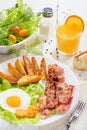 English breakfast-plate with fried bacon, with French fries, fried egg stands on a white table