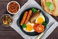 English breakfast: sausages, bacon, tomatoes, egg, beans in sauce, fried mushrooms, toast on a dark wooden background Royalty Free Stock Photo