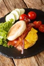 English freshly baked muffin sandwiches with scrambled eggs, bacon, cheese and vegetables close-up on a slate board. vertical Royalty Free Stock Photo