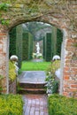 English garden gate with a marmoreal sculpture between shrubs of box trees