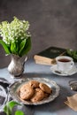 English 5 o`clock tea. Oat cookies or biscuits on a vintage plate, a cup of black tea, books and may-lily bouquet on dark