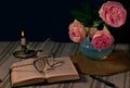 English rose in a vase on a table next to an open book with glasses for reading and a burning candle with a dark background Royalty Free Stock Photo