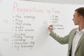 English teacher giving lesson on prepositions of time near whiteboard in classroom