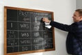 English teacher giving lesson on tenses near blackboard in classroom