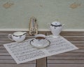 English teacup with saucer, cream jug and sugar bowl, fine bone china porcelain, and a metronome for music on a sheet of music