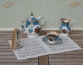 English teacup with saucer, teapot and cream jug, and a metronome for music on a sheet of music