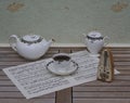 English teacup with saucer, teapot and sugar bowl, fine bone china porcelain, and a metronome for music on a sheet of music