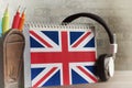 An English textbook on a spiral and headphones hanging from the side, a stand with pencils stand on a wooden surface. Close-up,