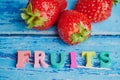 The English word fruits laid with wooden colored letters in front of strawberries against blue background