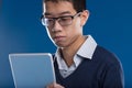 Engrossed Asian man checks tablet, blue backdrop