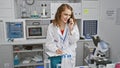 Engrossed young woman scientist taking notes while discussing research over smartphone in busy lab