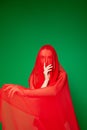 Mysterious woman covered with red veil against green background