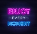 Enjoy every moment neon inspirational quote on a brick wall.